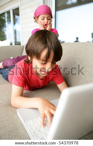 Portrait of a little boy and a little girl on a sofa in front of a laptop computer