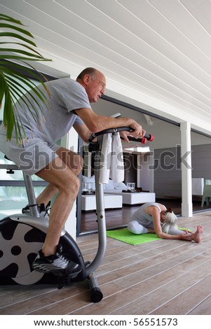 Elderly man making bike near a woman doing fitness