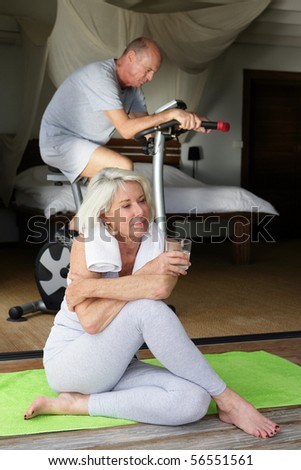 Elderly woman resting with a glass of water near a man doing bike