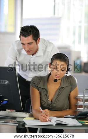 Young man in suit in front of a desktop computer near a young woman with headset