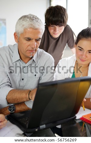 Portrait of a man and teenagers in front of a laptop computer in a classroom