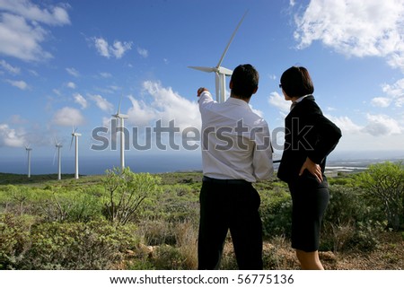 Young man and young woman in suit face to a wind turbine