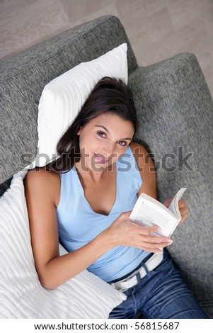 Portrait of a smiling young woman laid on a sofa reading a book