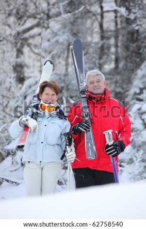 Senior man and woman smiling with skis in snow