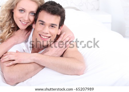 Man and woman smiling laid on a bed