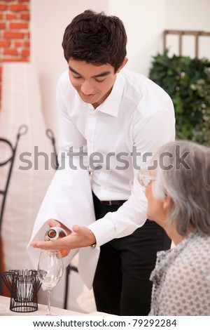 Young waiter serving an older customer rose wine