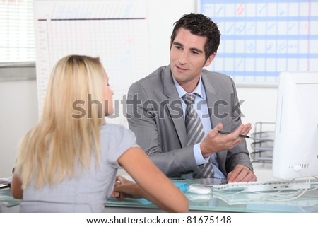 Suited man talking to a young woman across a desk