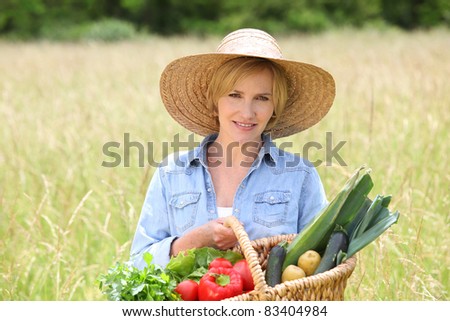 Woman in straw hat with basket of vegetables walking through a field