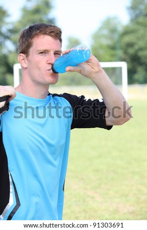 Man stood by soccer pitch drinking energy drink