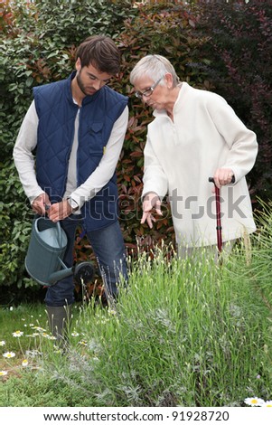 young man watering plants with older woman