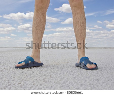 tanned legs of man wearing flip flops standing on the beach