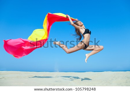 Fit young lady jumping in the sky with colorful fabric