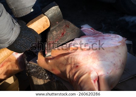 A butcher uses an axe to cut raw pork ready to sell
