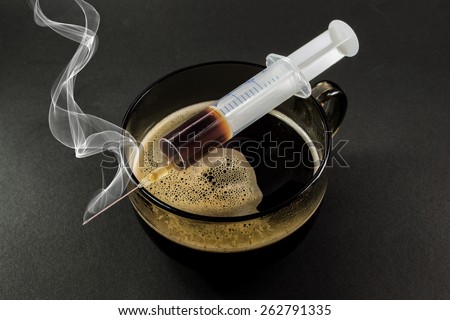 A full hypodermic needle rests on top of a glass cup of coffee