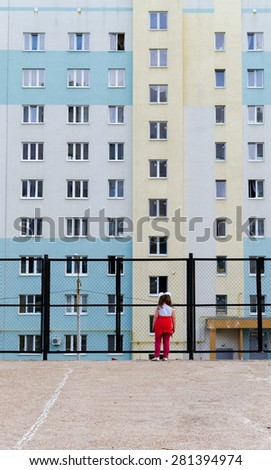 Single girl looking through a fence at apartment block