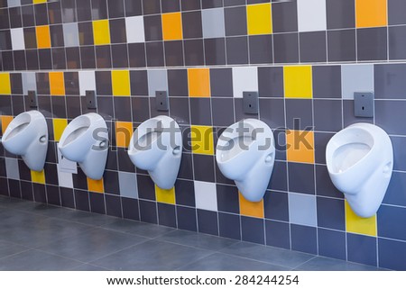White porcelain urinals against a yellow and orange tiled wall