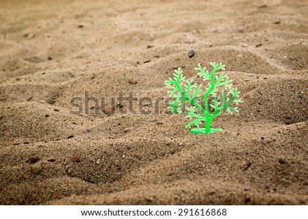 Single green plastic tree stands alone in a sand pit