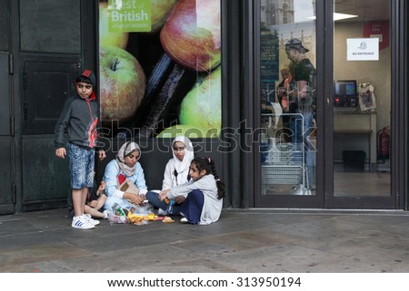 18th August 2015 - Family group sits on the ground eats outside a local shop displaying Best of British advert outside the busy Big Ben attraction in London