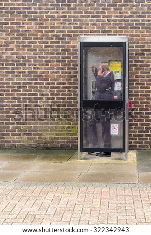 WITHAM - ENGLAND 1ST SEPTEMBER 2015 - Man in a suit uses an modern British telephone box to make an important  call in Witham England during September 2015
