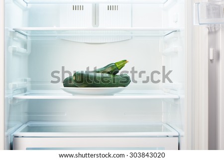 Two green zucchini on white plate in open empty refrigerator. Weight loss diet concept.