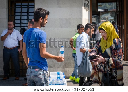 Istanbul, Turkey - September 05, 2015: Crowds of people walking on the street near Eminonu port in Istanbul. Old lady is buying cold water in a sunny Summer day from illegal street vendor.