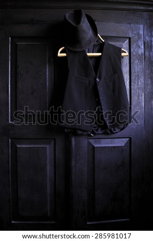 A black waistcoat on a wooden hanger and a black hat on it