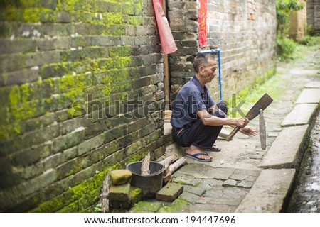 GUANGZHOU, CHINA - MAY 19: An unidentified old village man is preparing wood for cooking at the hallway in a very old village near Guangzhou, China on May 19 2014.