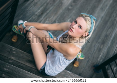 adult female skater on wood steps on stake board wearing shorts headband and tank top staring at the camera