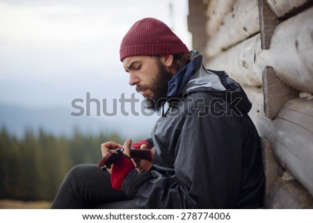 bearded guy playing guitar in mountains near wooden house
