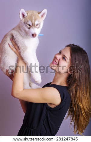 young caucasian female playing with a puppy, girl and siberian husky studio shot on grey background