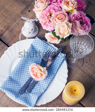 Beautiful festive table setting with roses, candles, shiny new cutlery and napkins on a vintage wooden background