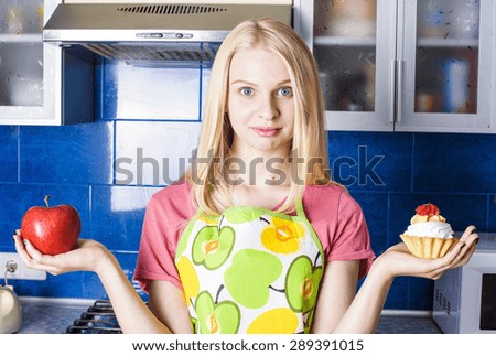 young caucasian woman trying to choose cupcake or apple on kitchen, healthy lifestyle concept