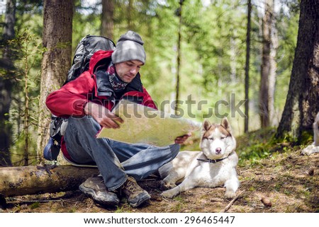 young caucasian male with a map and siberian husky dog in the forest, hiker looking at map outdoors