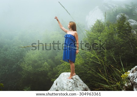 young caucasian female posing in blue dress in mountains in foggy weather