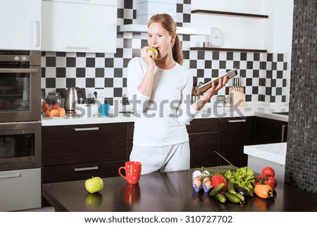 young caucasian female on kitchen with apple and tablet. Woman on kitchen searching on tablet recipes of healthy food. Cooking healthy food with vegetables and fruits
