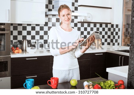 young caucasian female on kitchen with apple and tablet. Woman on kitchen searching on tablet recipes of healthy food. Cooking healthy food with vegetables and fruits