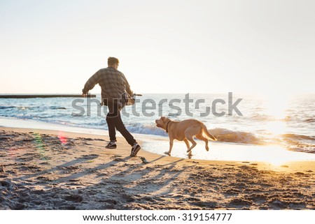 young caucasian male playing with labrador on beach during sunrise or sunset. Man and dog having fun on seaside