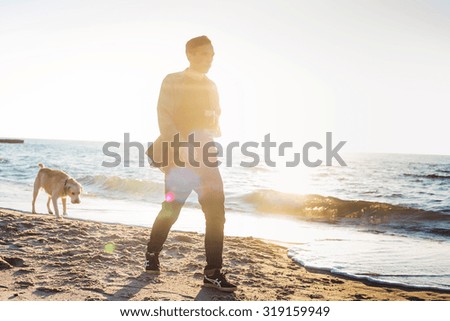 young caucasian male playing with labrador on beach during sunrise or sunset. Man and dog having fun on seaside