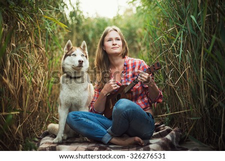 young caucasian woman playing ukulele. Female with siberian husky dog playing guitar outdoors