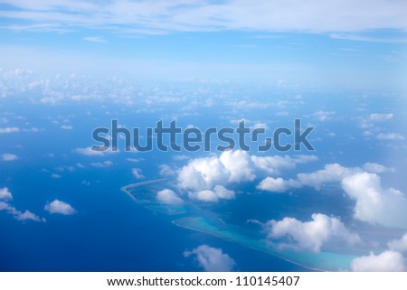 The atoll ring at ocean is visible through clouds. Aerial view.