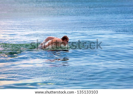 young sporting man swims in the sea dolphin style