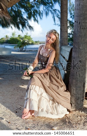 The young beautiful woman in a romantic dress on a bench on a beach, tropics