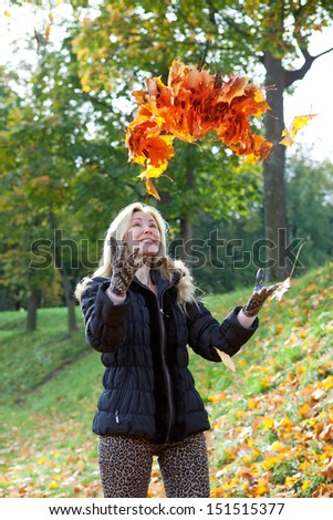 The beautiful woman in autumn park throws up red maple leaves