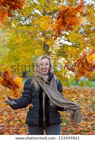 The beautiful woman in autumn park throws up red maple leaves