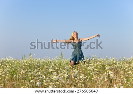 The happy young woman jumps in the field  of camomiles