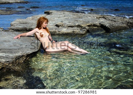 The young beautiful woman in a natural sea swimming bath among stones.