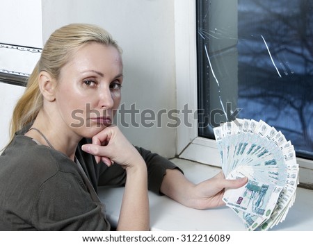 The sad young woman counts money for window repair with the burst, broken glass
