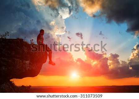 One guy sits on a rock and looking at pink sunset
