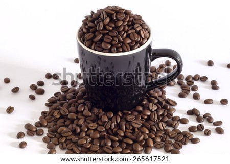 Black mug filled of coffee beans and some more over the table