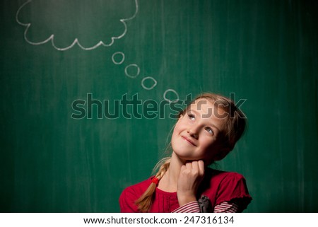 Little girl standing in front of chalkboard with comic cloud drawing on it and she looks pensive but happy
